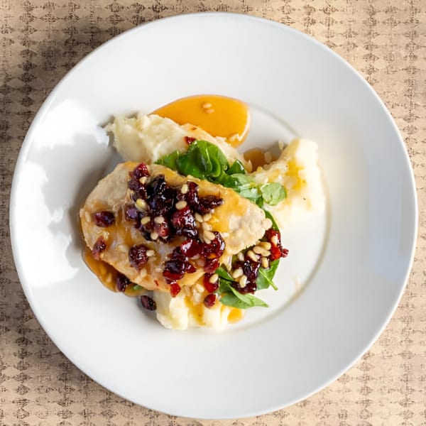 Chicken with cranberry sauce, pine nuts, and mashed potatoes on a white plate.