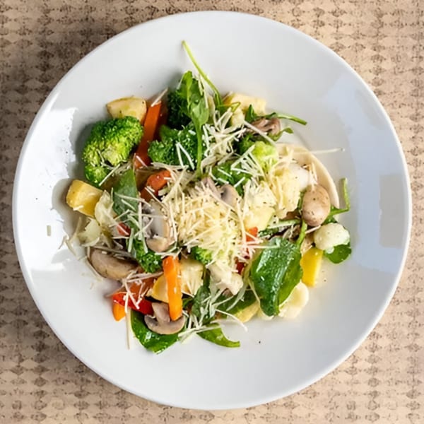 Colorful vegetable medley with broccoli, carrots, mushrooms, and cheese on a white plate.