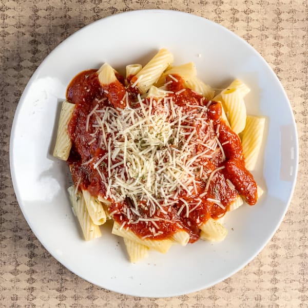 Rigatoni pasta with red sauce, grated cheese, and herbs on a white plate.