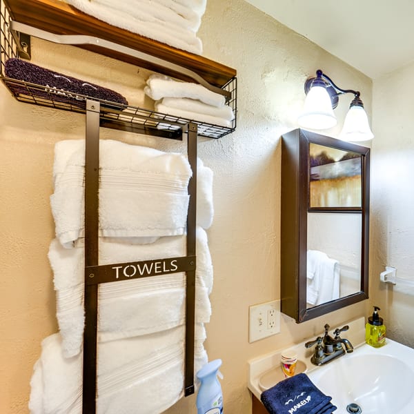 A bathroom with a sink, mirror, light fixture, and a towel rack with white towels.