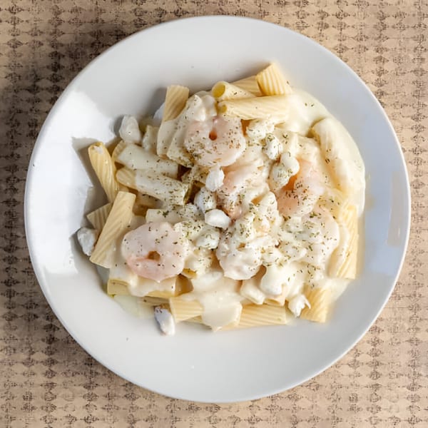 Creamy pasta dish with rigatoni, shrimp, and crab meat, topped with herbs on a white plate.