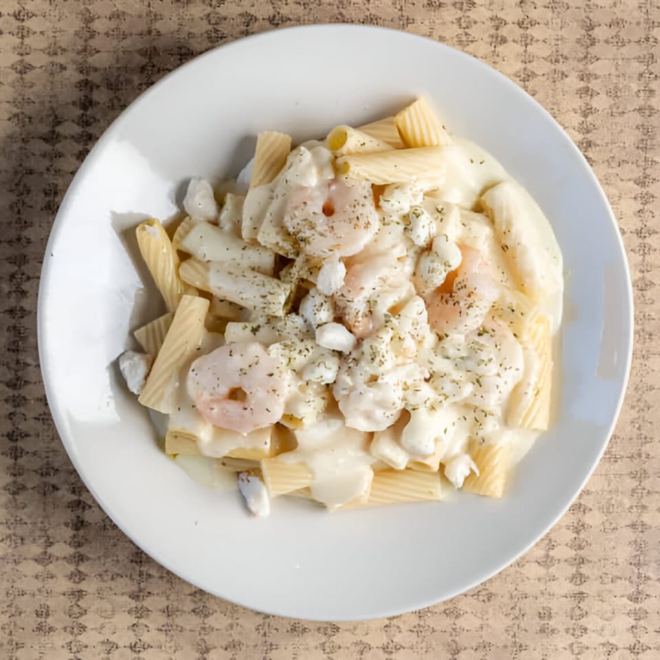 Creamy pasta dish with rigatoni, shrimp, and crab meat, topped with herbs on a white plate.