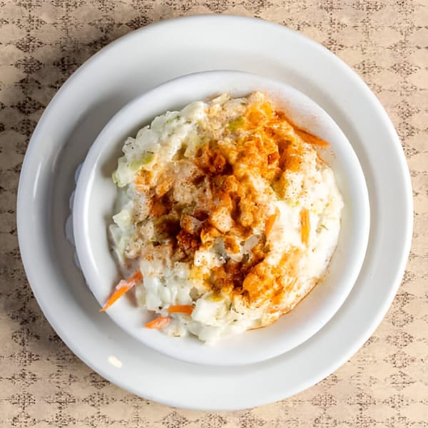 Creamy coleslaw with shredded cabbage, carrots, and a sprinkle of paprika in a white bowl.